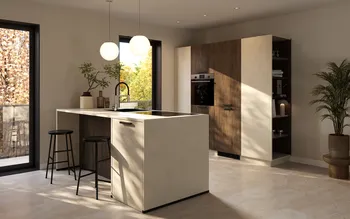 Helle, moderne Küche mit Kochinsel in Steinoptik, zwei schwarzen Barhockern und runden Pendelleuchten; schwarze Fensterrahmen mit Blick ins Grüne, Hochschrankwand in Holz und Beige mit integriertem Backofen sowie offenes Regal und Zimmerpflanze.